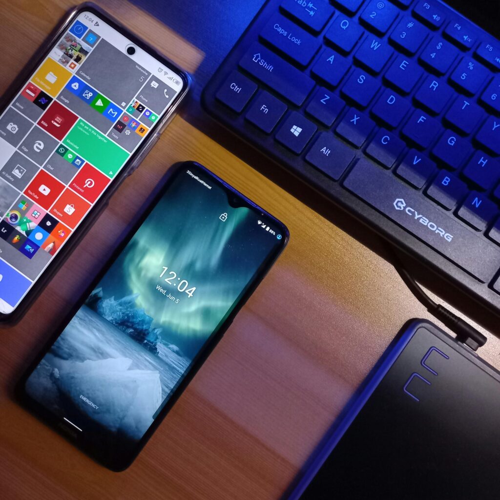 Two smartphones alongside a keyboard on a wooden desk showcasing technology.
