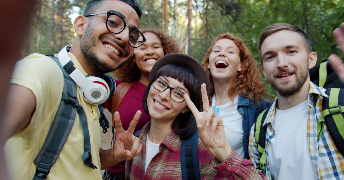 Group of diverse friends hiking and laughing in a forest setting.